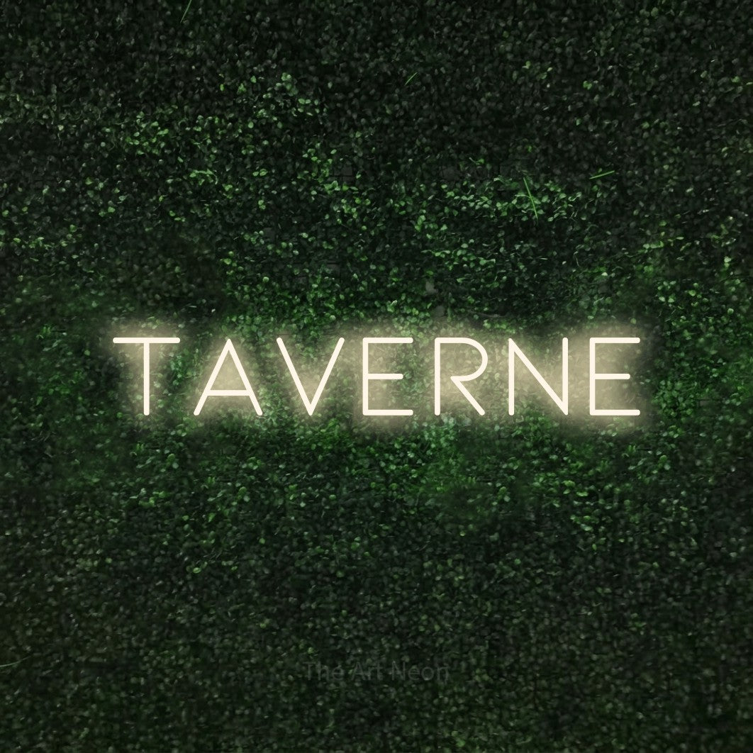 Décoration murale en néon LED « Taverne » en blanc chaud, en lettres fines et espacées, installée sur une haie verte texturée, pour un bar à la maison.