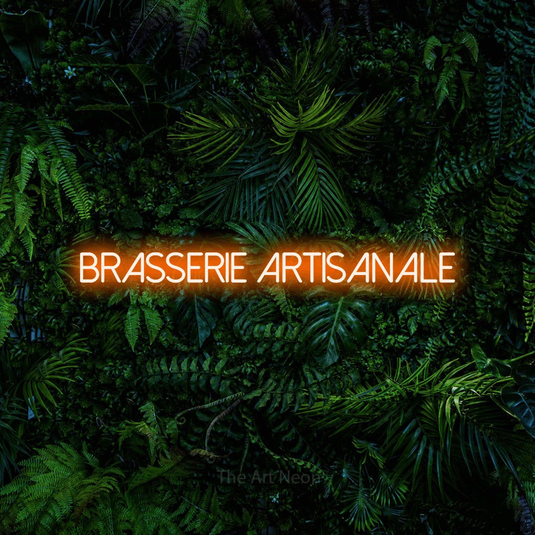 “Brasserie artisanale” LED neon sign in orange, with thin sans-serif lettering, shown against dense tropical foliage.