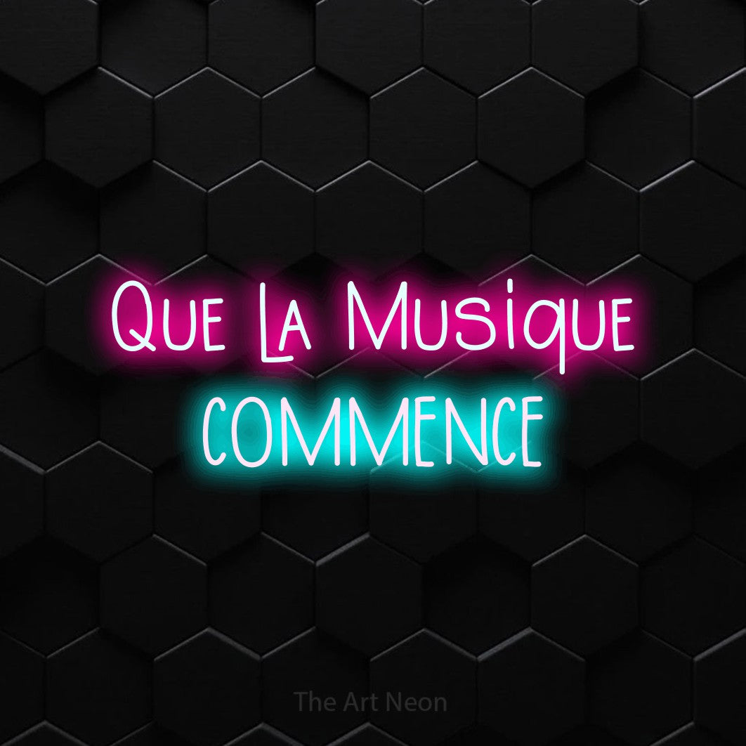 “Que la musique commence” LED neon sign in hot pink on the upper line and ice blue on the lower line, with narrow hand-drawn lettering across 2 lines, shown against black hexagonal wall tiles.
