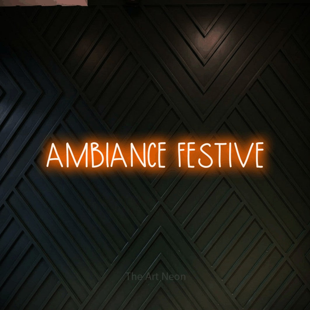 “Ambiance festive” LED neon sign in orange, with narrow hand-drawn lettering, shown against a black chevron-patterned wood wall.