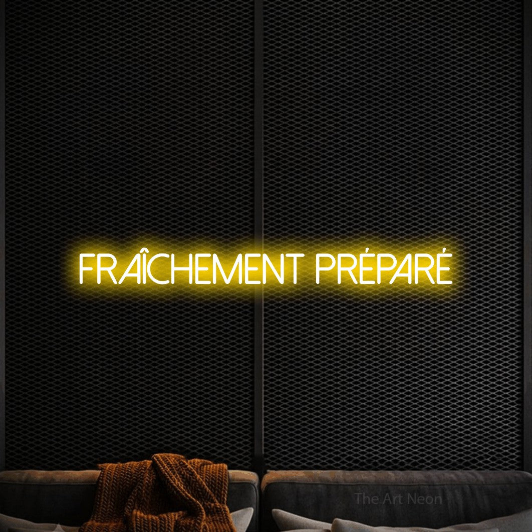 “Fraîchement préparé” LED neon sign in yellow, with thin sans-serif lettering, shown against a modern dark-toned seating area.