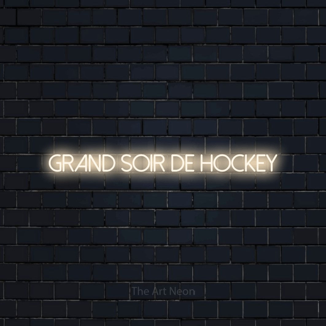 “Grand soir de hockey” LED neon sign in warm white, with thin sans-serif lettering, shown against a dark navy brick wall.