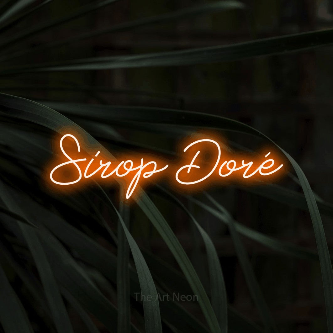 “Sirop doré” LED neon sign in orange, with cursive lettering, shown against a close-up of dark foliage.