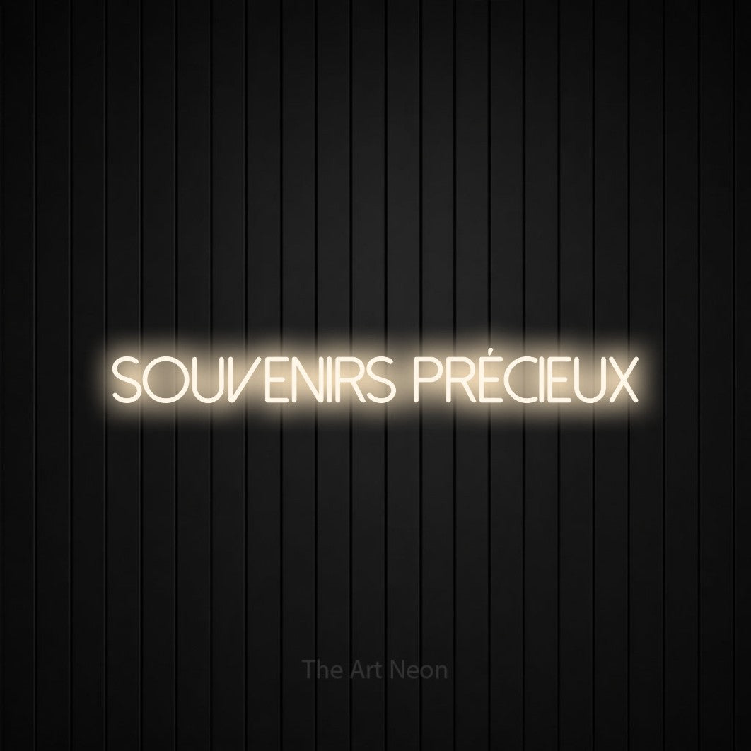 “Souvenirs précieux” LED neon sign in warm white, with thin sans-serif lettering, shown against black vertical wall slats.