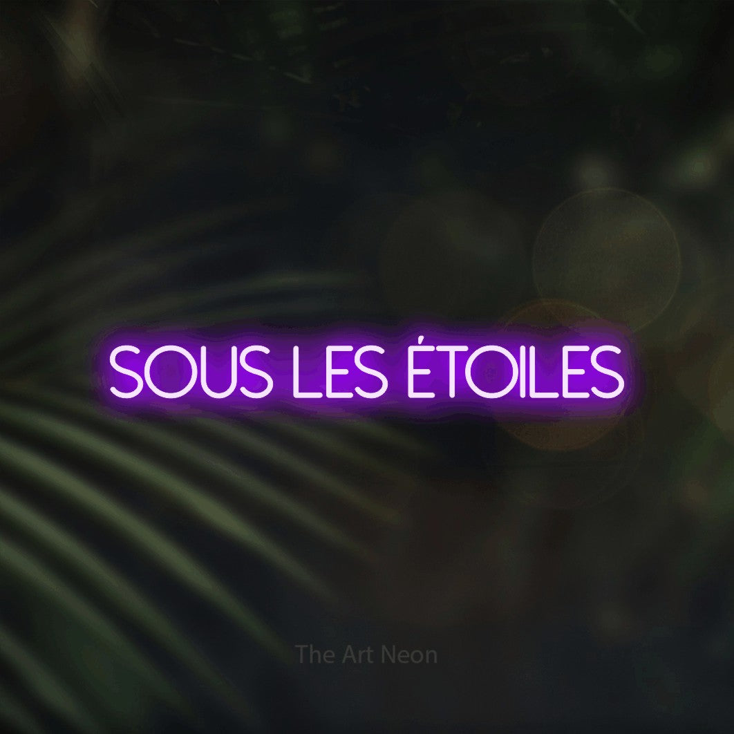 “Sous les étoiles” LED neon sign in purple, with thin sans-serif lettering, shown against a blurred palm and bokeh-light backdrop.