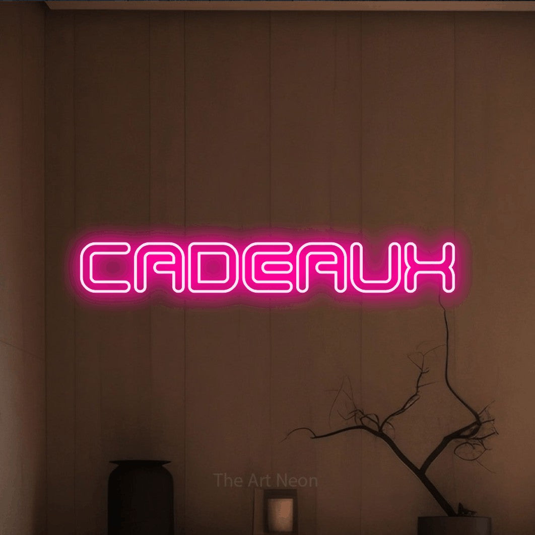 “Cadeaux” LED neon sign in hot pink, with futuristic double-line lettering, shown against a simple earth-toned interior.