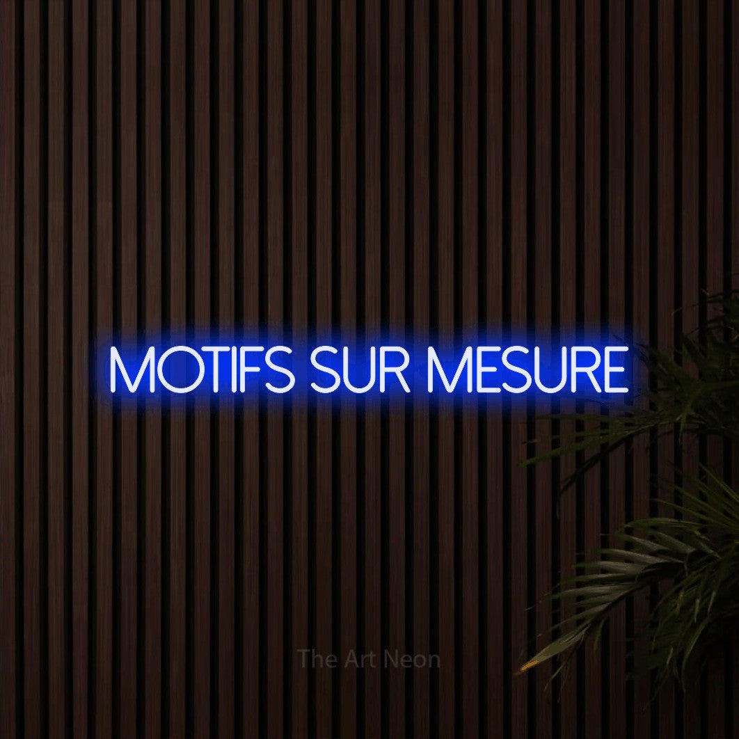 “Motifs sur mesure” LED neon sign in blue, with thin sans-serif lettering, shown against dark wooden wall slats.