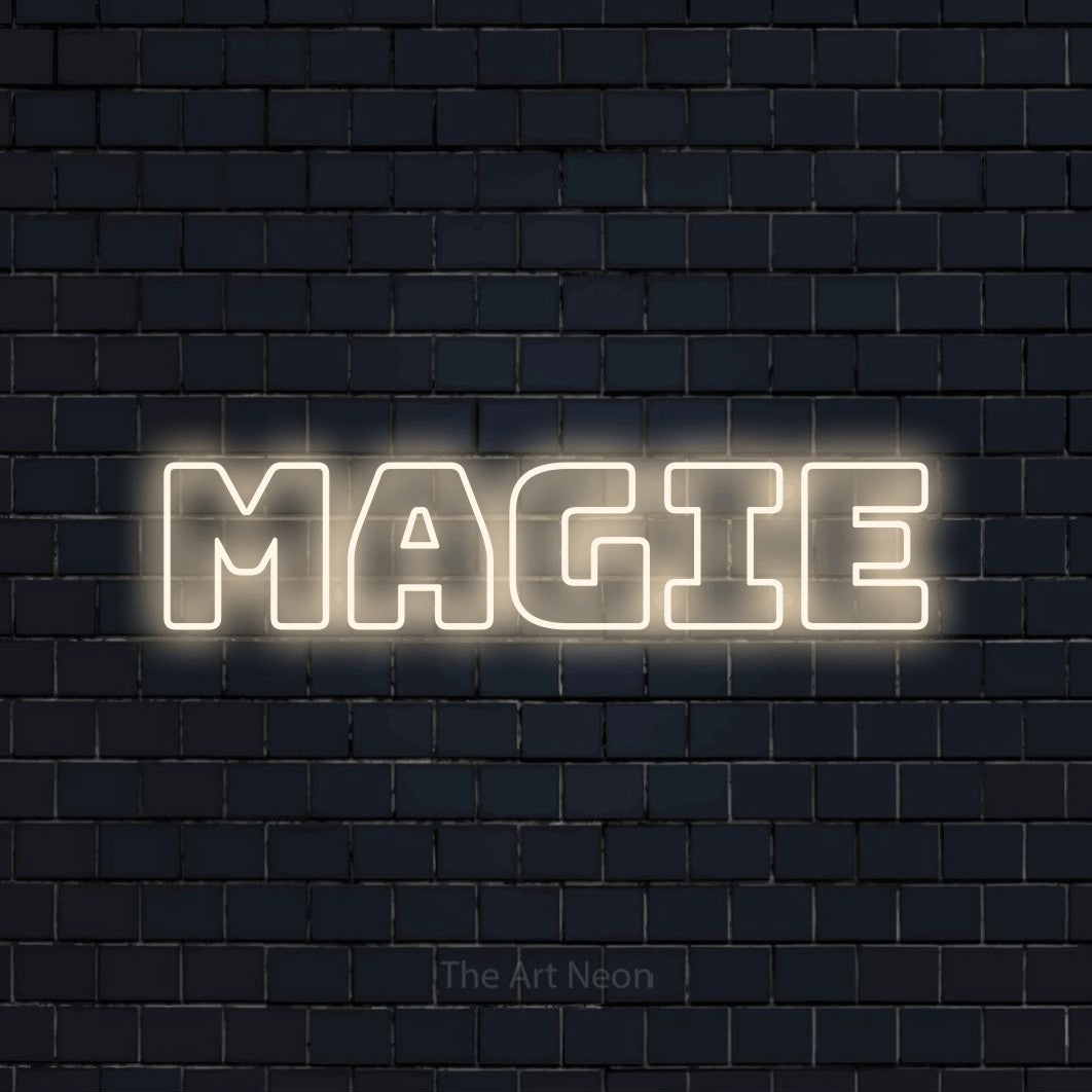 “Magie” LED neon sign in warm white, with bold outline lettering, shown against a dark navy brick wall.