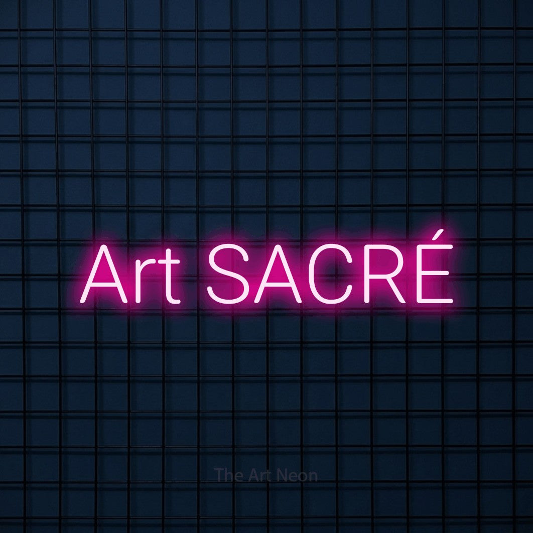 “Art sacré” LED neon sign in hot pink, with rounded sans-serif lettering, shown against a dark blue grid.