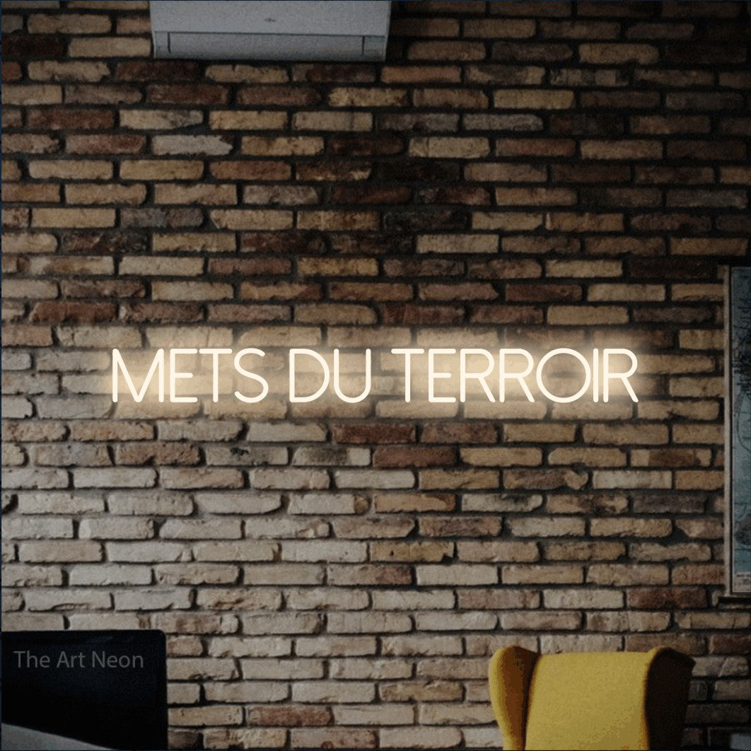 “Mets du terroir” LED neon sign in warm white, with thin sans-serif lettering, shown against warm-toned brickwork.