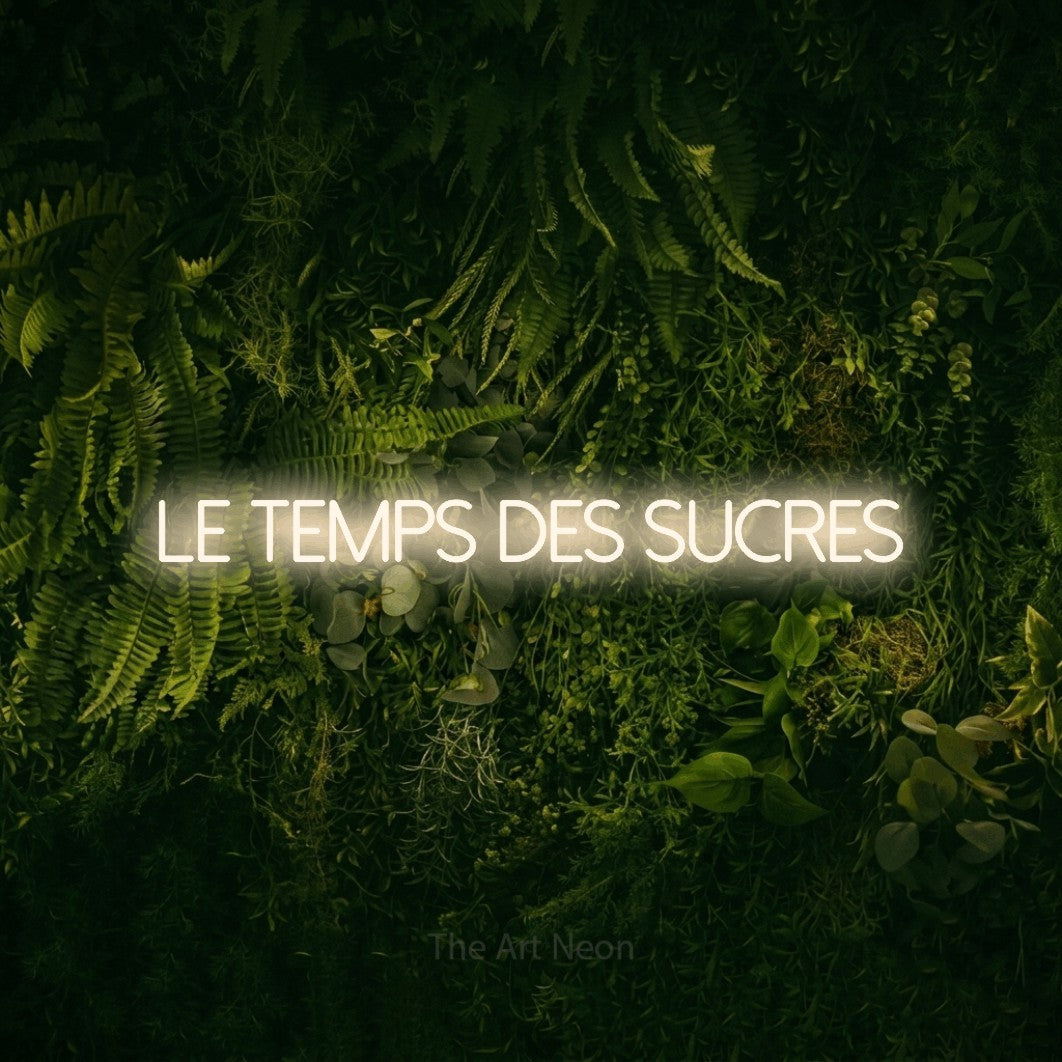 “Le temps des sucres” LED neon sign in warm white, with thin sans-serif lettering, shown against a dark moss and forest backdrop.