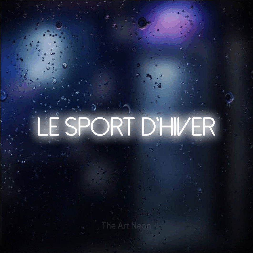 “Le sport d'hiver” LED neon sign in cool white, with thin sans-serif lettering, shown against glass with blue and purple reflections.
