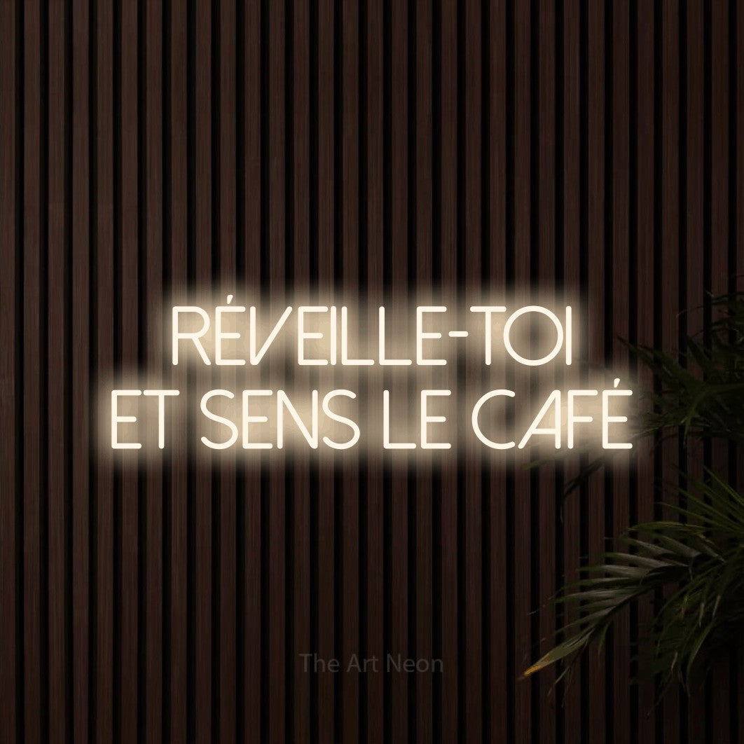 Décoration murale en néon LED « Réveille-toi et sens le café » sur deux lignes en blanc chaud, en lettres fines sans empattement, installée sur un mur de lattes en bois foncé, pour un café.