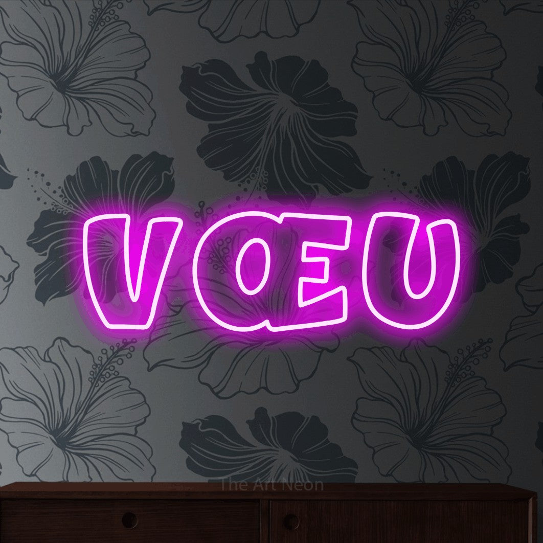 “Vœu” LED neon sign in pink, with rounded outline lettering, shown against a grey floral-patterned wall.