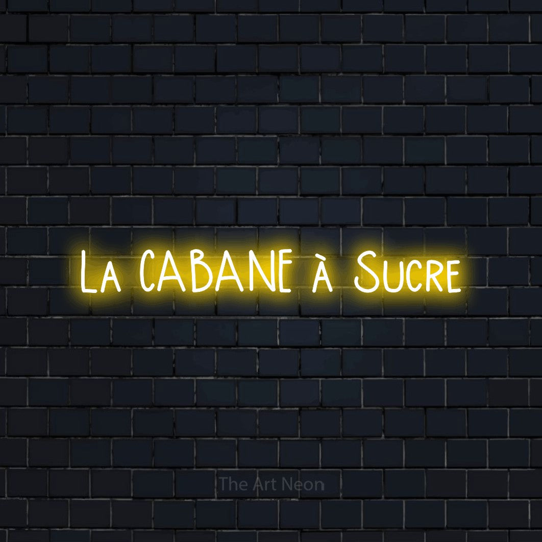 “La cabane à sucre” LED neon sign in yellow, with narrow hand-drawn lettering, shown against a dark navy brick wall.