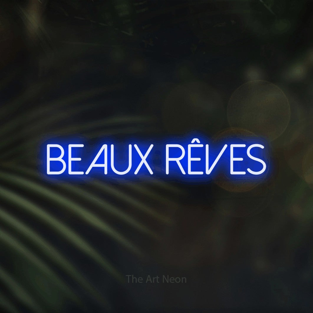 “Beaux rêves” LED neon sign in blue, with thin sans-serif lettering, shown against a blurred palm and bokeh-light backdrop.