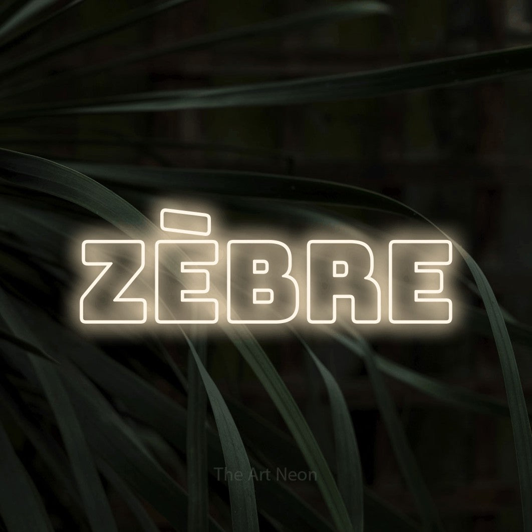 “Zèbre” LED neon sign in warm white, with bold outline lettering, shown against a close-up of dark foliage.