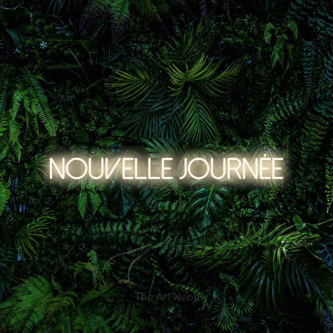 “Nouvelle journée” LED neon sign in warm white, with thin sans-serif lettering, shown against dense tropical foliage.