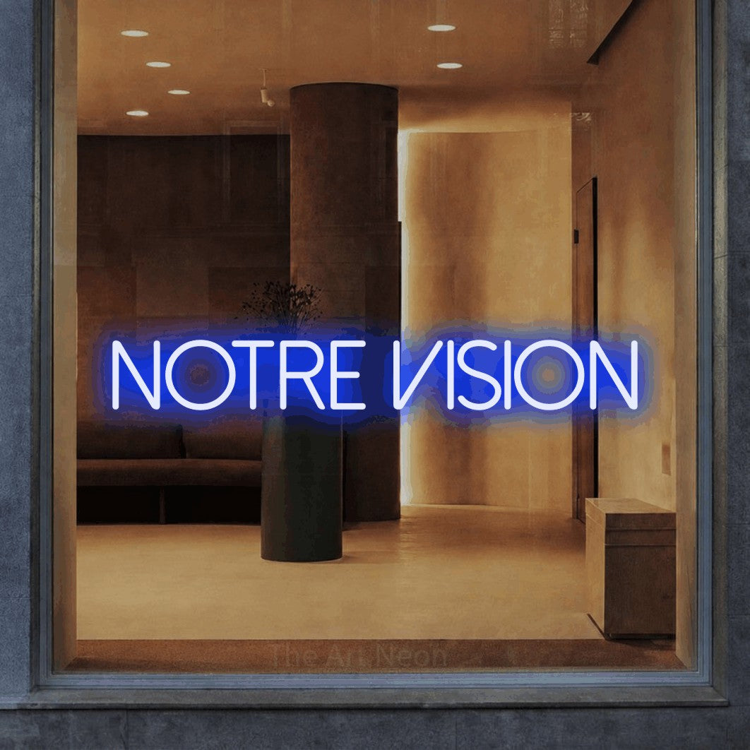 “Notre vision” LED neon sign in blue, with thin sans-serif lettering, shown against a warm-toned interior.