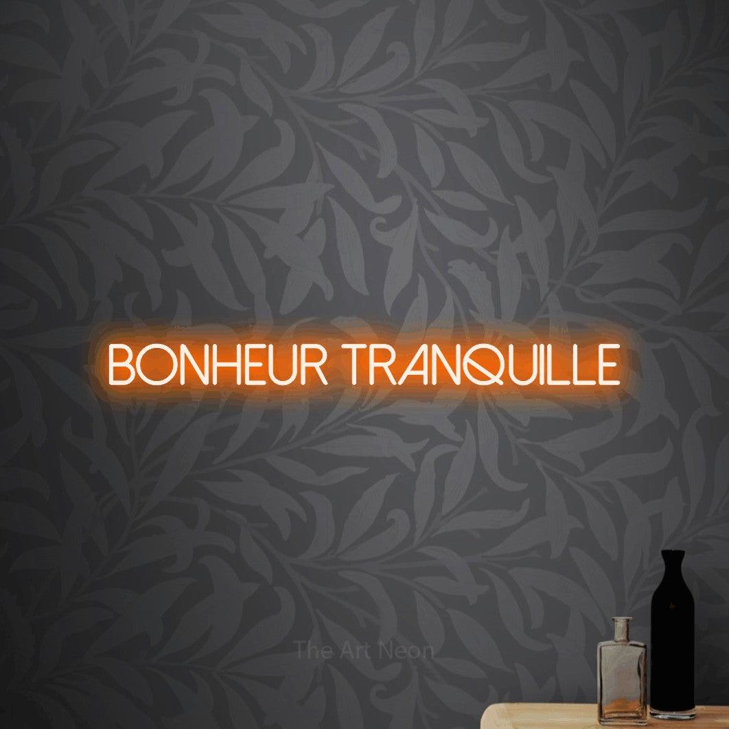 “Bonheur tranquille” LED neon sign in orange, with thin sans-serif lettering, shown against grey botanical wallpaper.