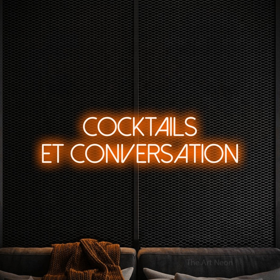 Décoration murale en néon LED « Cocktails et conversation » sur deux lignes en orange, en lettres fines sans empattement, installée dans un coin salon moderne aux tons noirs, pour un bar ou un pub.