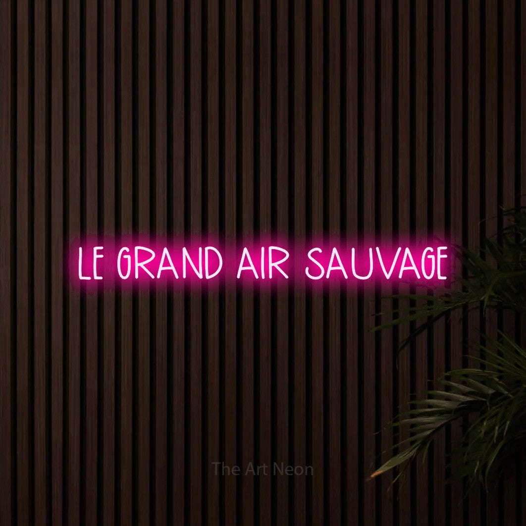 “Le grand air sauvage” LED neon sign in hot pink, with narrow hand-drawn lettering, shown against dark wooden wall slats.