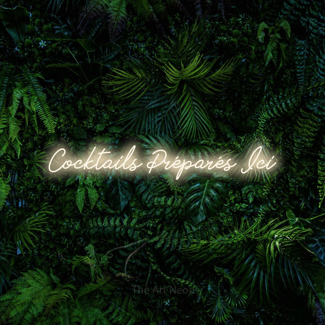 “Cocktails préparés ici” LED neon sign in warm white, with cursive lettering, shown against dense tropical foliage.