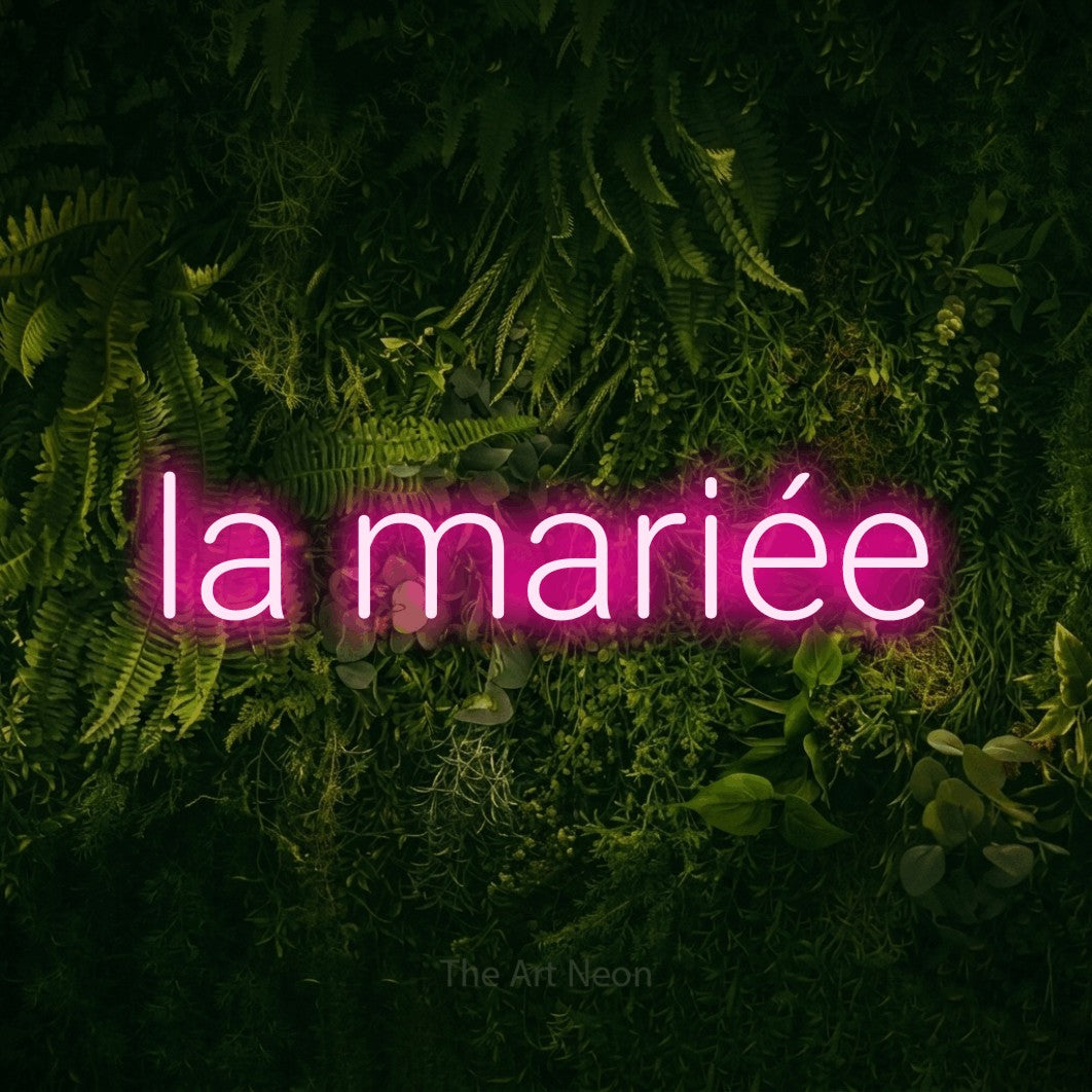 “La mariée” LED neon sign in hot pink, with rounded sans-serif lettering, shown against a dark moss and forest backdrop.