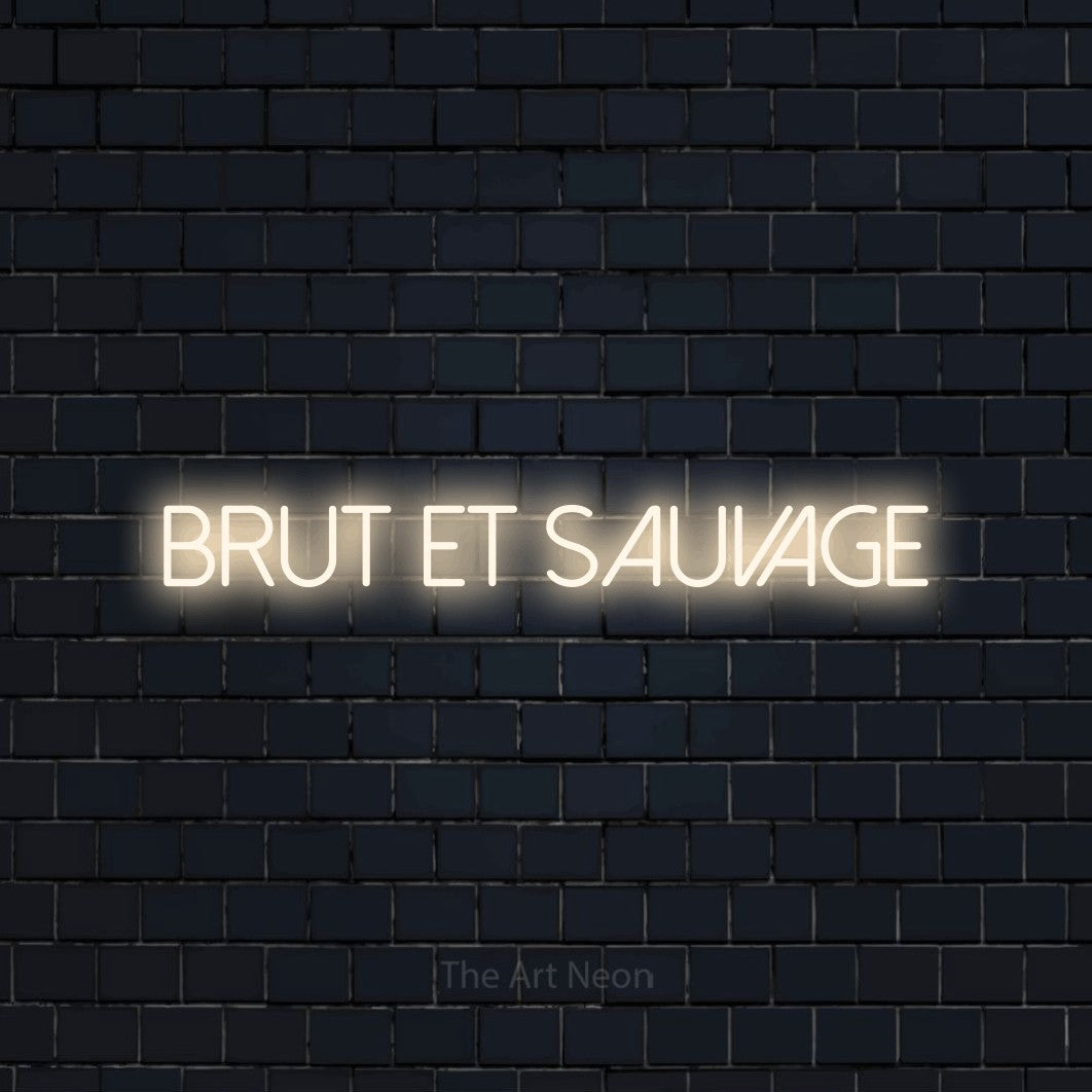 “Brut et sauvage” LED neon sign in warm white, with thin sans-serif lettering, shown against a dark navy brick wall.