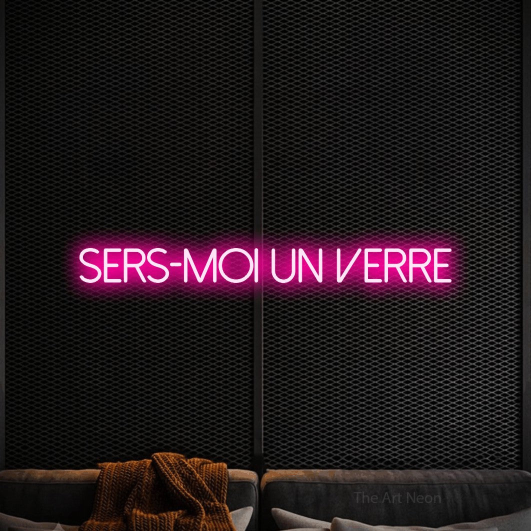 Aperçu d’une enseigne néon LED « Sers-moi un verre » en rose vif, en lettres fines sans empattement, photographiée dans un coin salon moderne aux tons noirs, pour un bar à la maison.