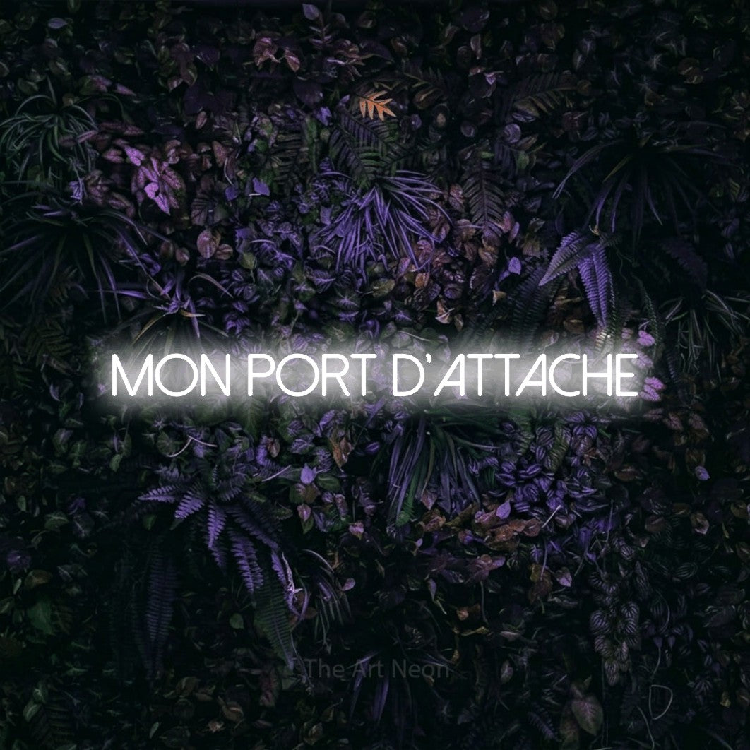 “Mon port d'attache” LED neon sign in cool white, with thin sans-serif lettering, shown against a dark wall with purple flowers.