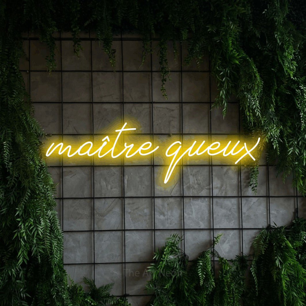 “Maître queux” LED neon sign in yellow, with cursive lettering, shown against an ivy-covered concrete grid.