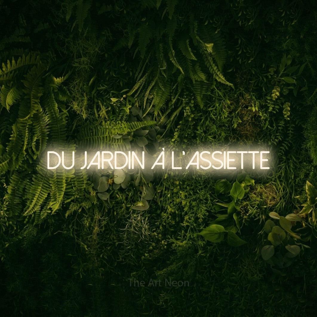 “Du jardin à l'assiette” LED neon sign in warm white, with thin sans-serif lettering, shown against a dark moss and forest backdrop.