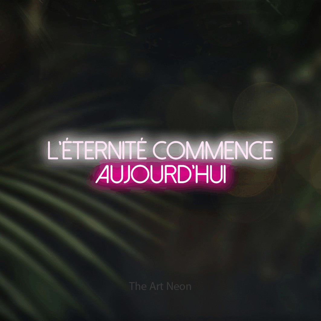 “L'éternité commence aujourd'hui” LED neon sign in cool white on the upper line and hot pink on the lower line, with thin sans-serif lettering across 2 lines, shown against a blurred palm and bokeh-light backdrop.