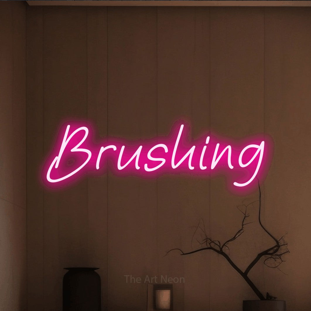 “Brushing” LED neon sign in hot pink, with slanted handwritten lettering, shown against a simple earth-toned interior.