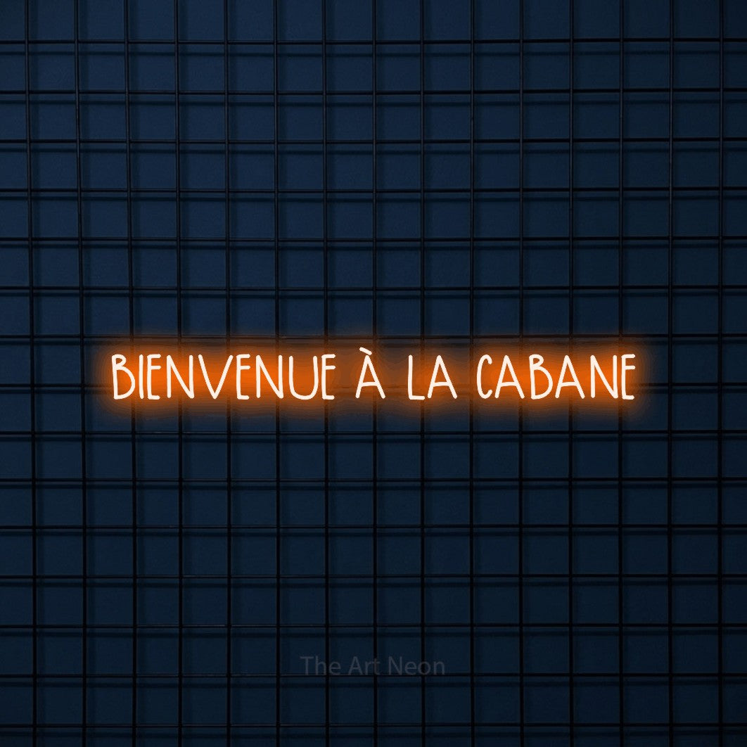 “Bienvenue à la cabane” LED neon sign in orange, with narrow hand-drawn lettering, shown against a dark blue grid.