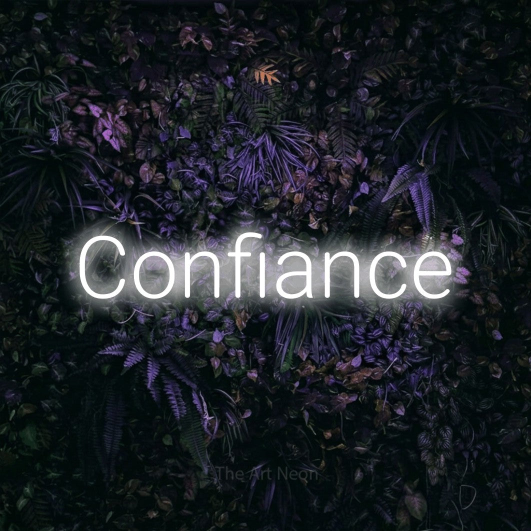Aperçu d’une enseigne néon LED « Confiance » en blanc froid, en lettres sans empattement arrondies, photographiée sur un mur sombre aux fleurs violettes, pour un salon de beauté.