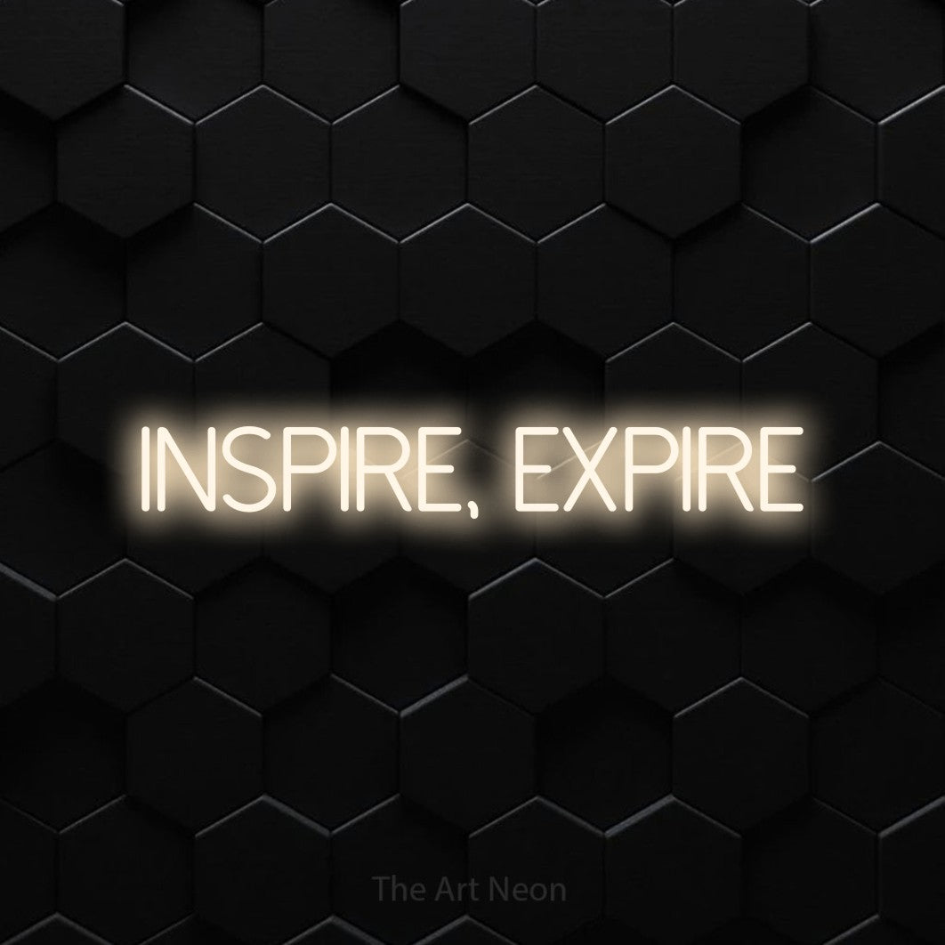 “Inspire, expire” LED neon sign in warm white, with thin sans-serif lettering, shown against black hexagonal wall tiles.