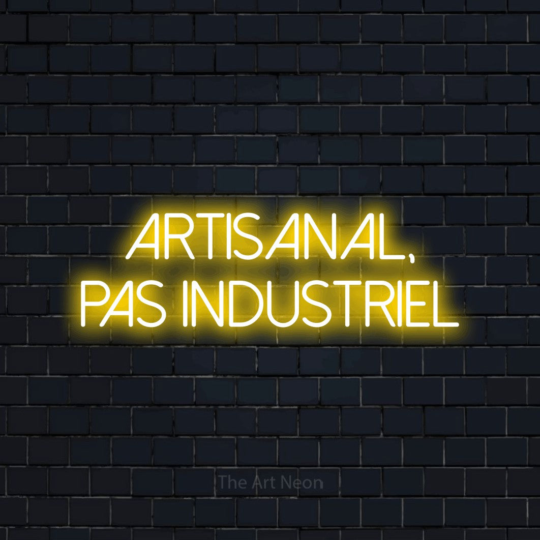 Néon LED « Artisanal, pas industriel » sur deux lignes en jaune, en lettres fines sans empattement, mis en scène sur un mur de briques bleu marine foncé, pour une microbrasserie.