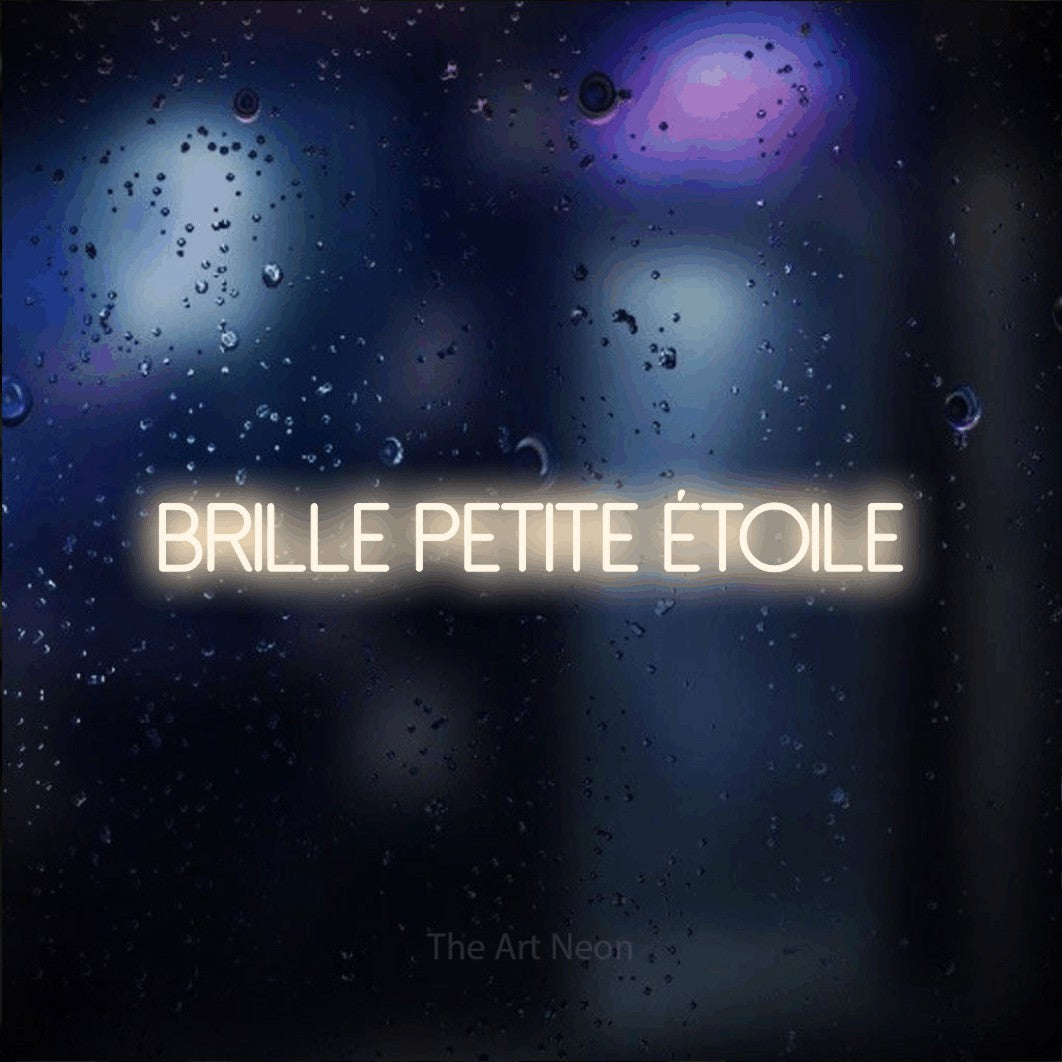 “Brille petite étoile” LED neon sign in warm white, with thin sans-serif lettering, shown against glass with blue and purple reflections.