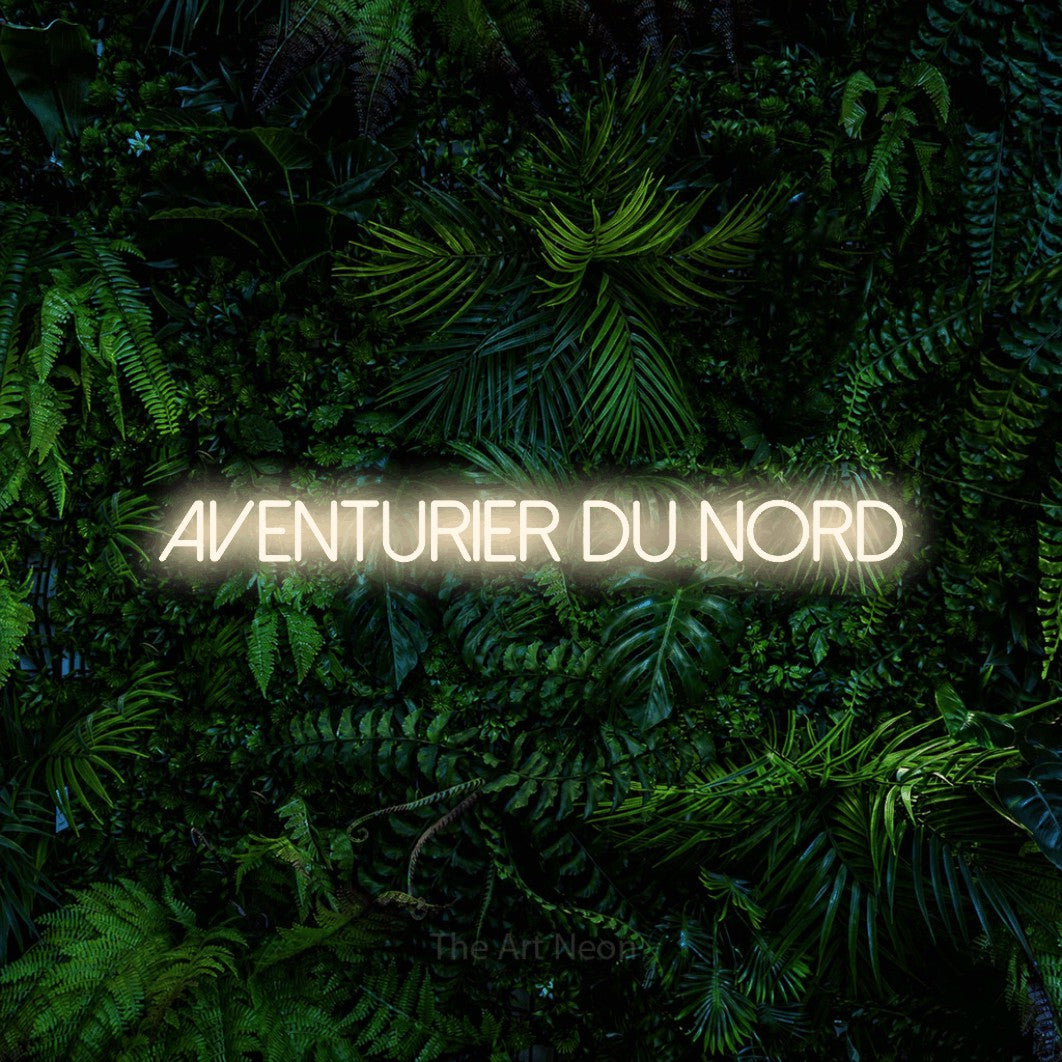 “Aventurier du nord” LED neon sign in warm white, with thin sans-serif lettering, shown against dense tropical foliage.