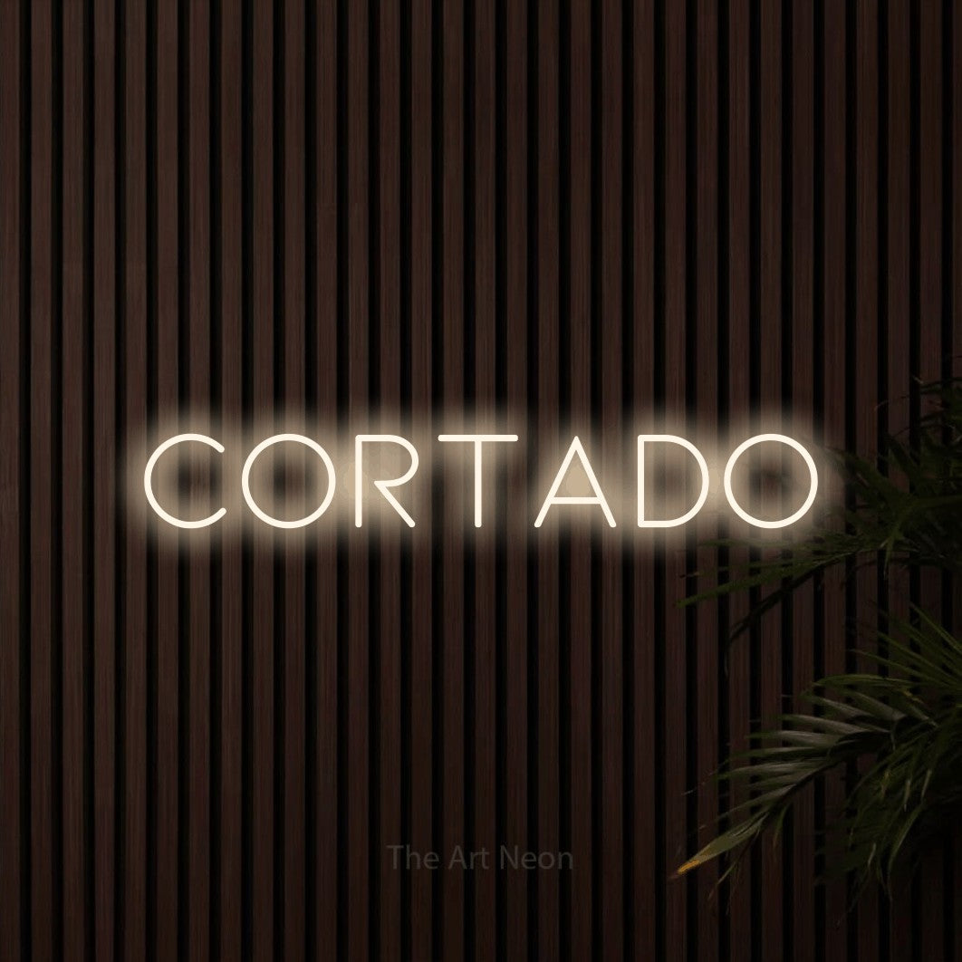 Néon LED « Cortado » en blanc chaud, en lettres fines et espacées, mis en scène sur un mur de lattes en bois foncé, pour un café.