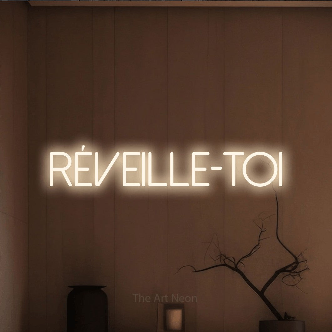 “Réveille-toi” LED neon sign in warm white, with thin sans-serif lettering, shown against a simple earth-toned interior.