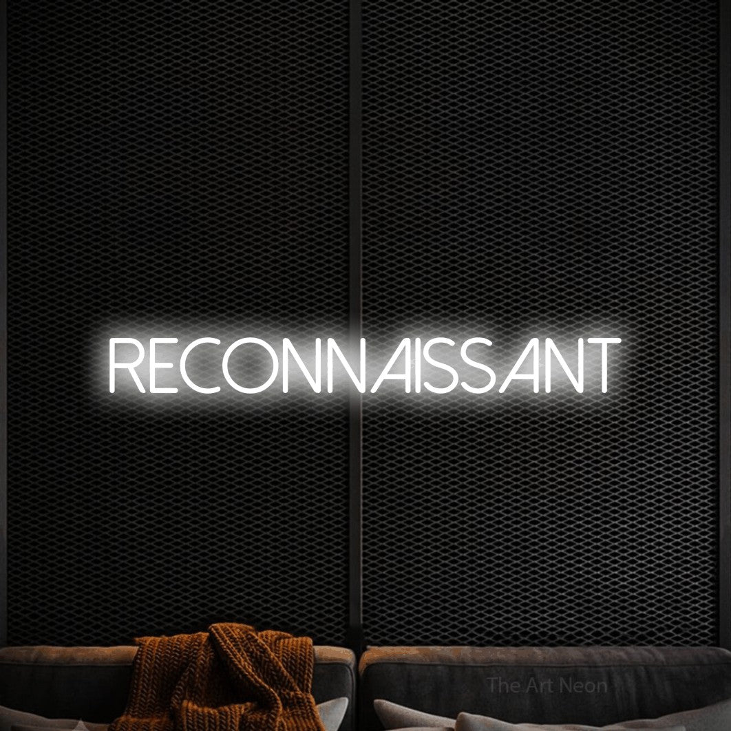Néon LED « Reconnaissant » en blanc froid, en lettres fines sans empattement, mis en scène dans un coin salon moderne aux tons noirs, pour un salon.