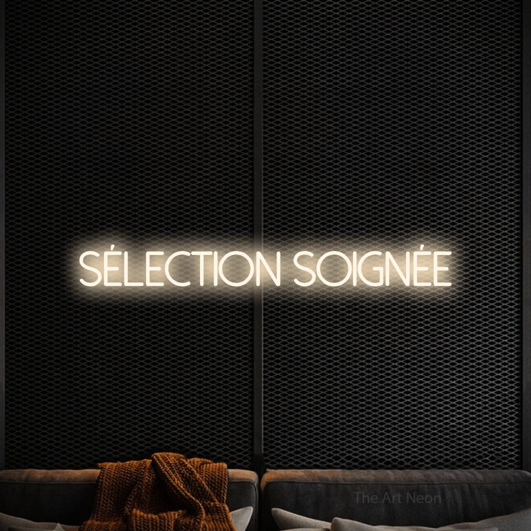 “Sélection soignée” LED neon sign in warm white, with thin sans-serif lettering, shown against a modern dark-toned seating area.