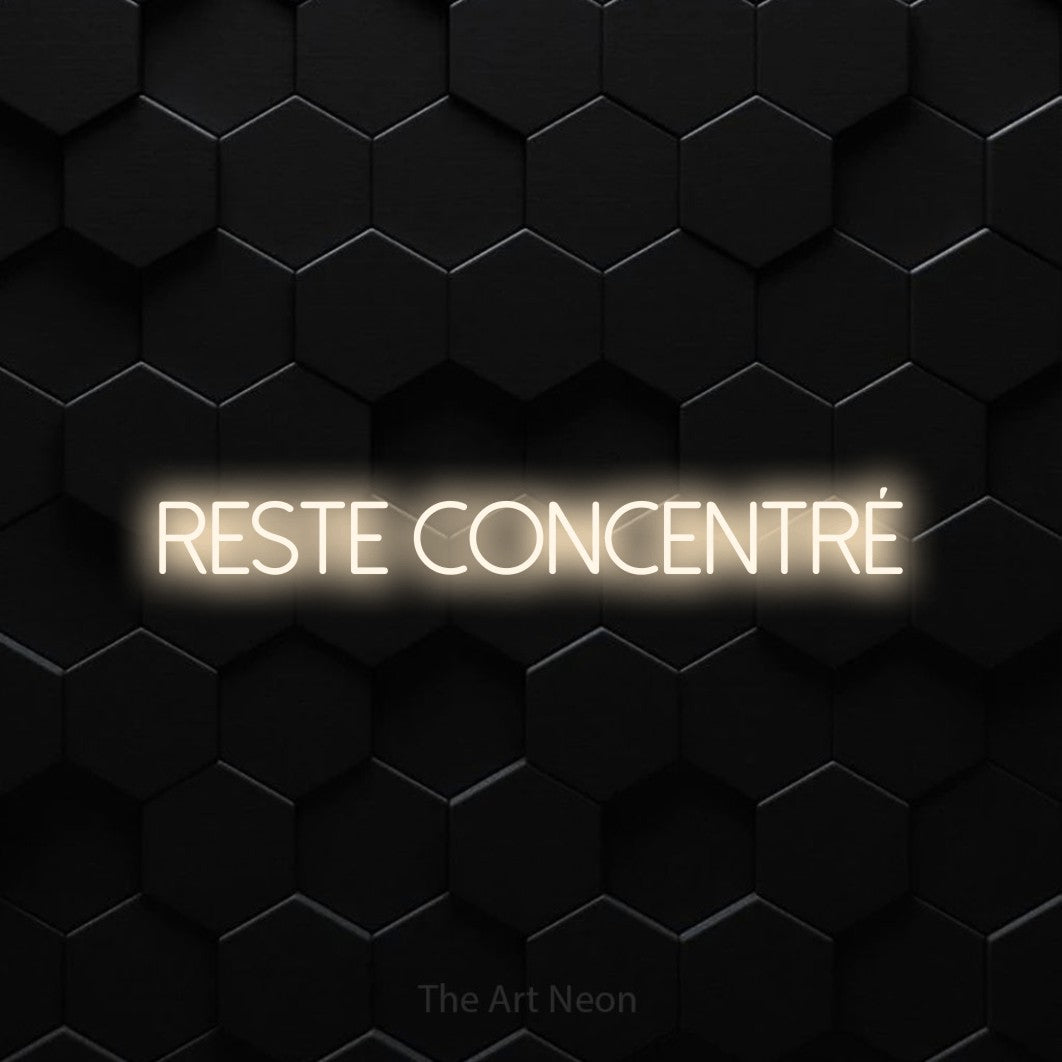 “Reste concentré” LED neon sign in warm white, with thin sans-serif lettering, shown against black hexagonal wall tiles.