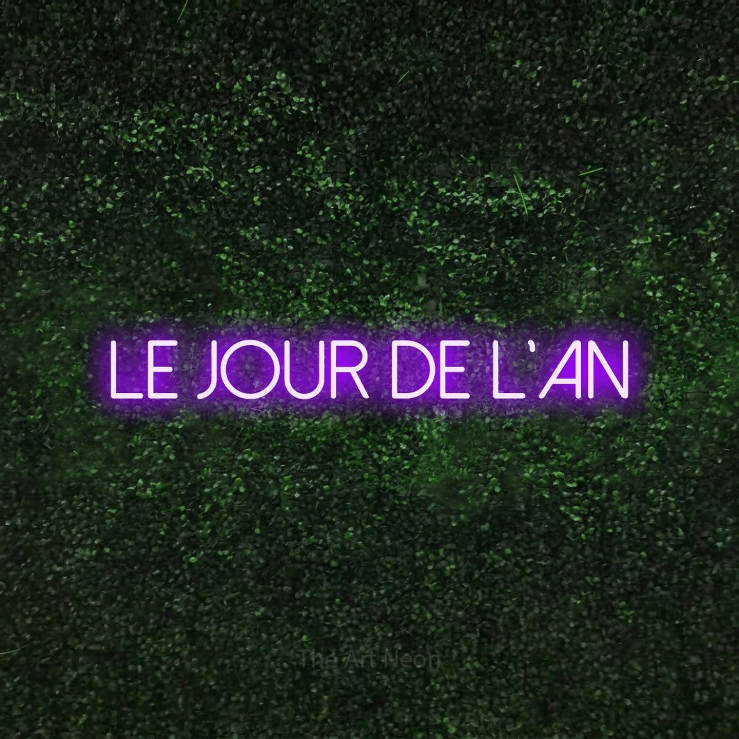 “Le jour de l'An” LED neon sign in purple, with thin sans-serif lettering, shown against a textured green hedge.