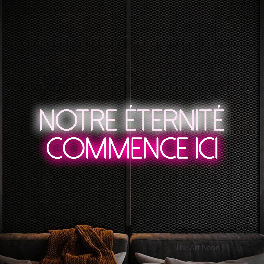 “Notre éternité commence ici” LED neon sign in cool white on the upper line and hot pink on the lower line, with thin sans-serif lettering across 2 lines, shown against a modern dark-toned seating area.