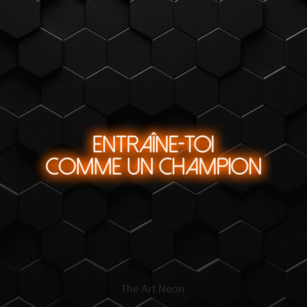 Lettrage en néon LED « Entraîne-toi comme un champion » sur deux lignes en orange, en lettres fines sans empattement, présenté sur un mur de carreaux hexagonaux noirs, pour un espace d’entraînement.