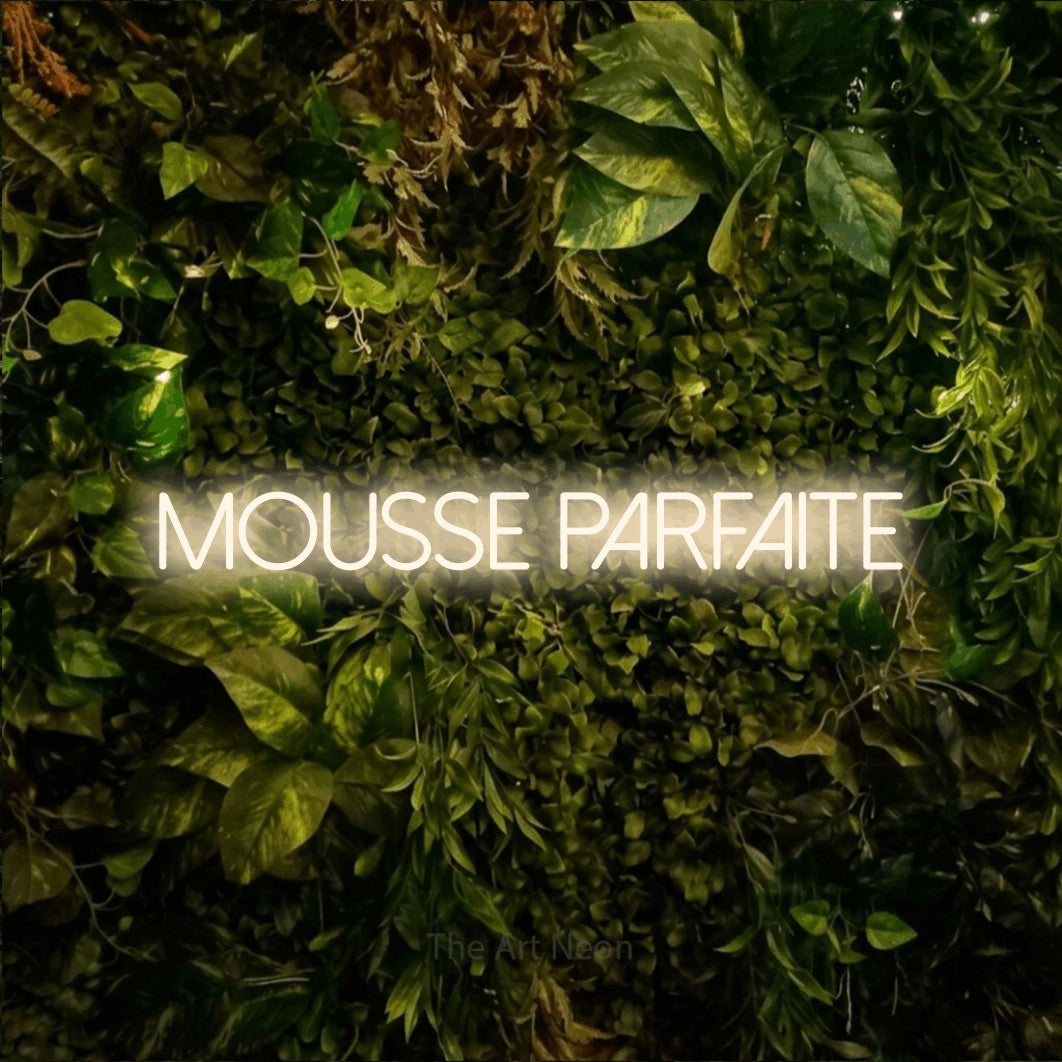 “Mousse parfaite” LED neon sign in warm white, with thin sans-serif lettering, shown against bright green and yellow foliage.